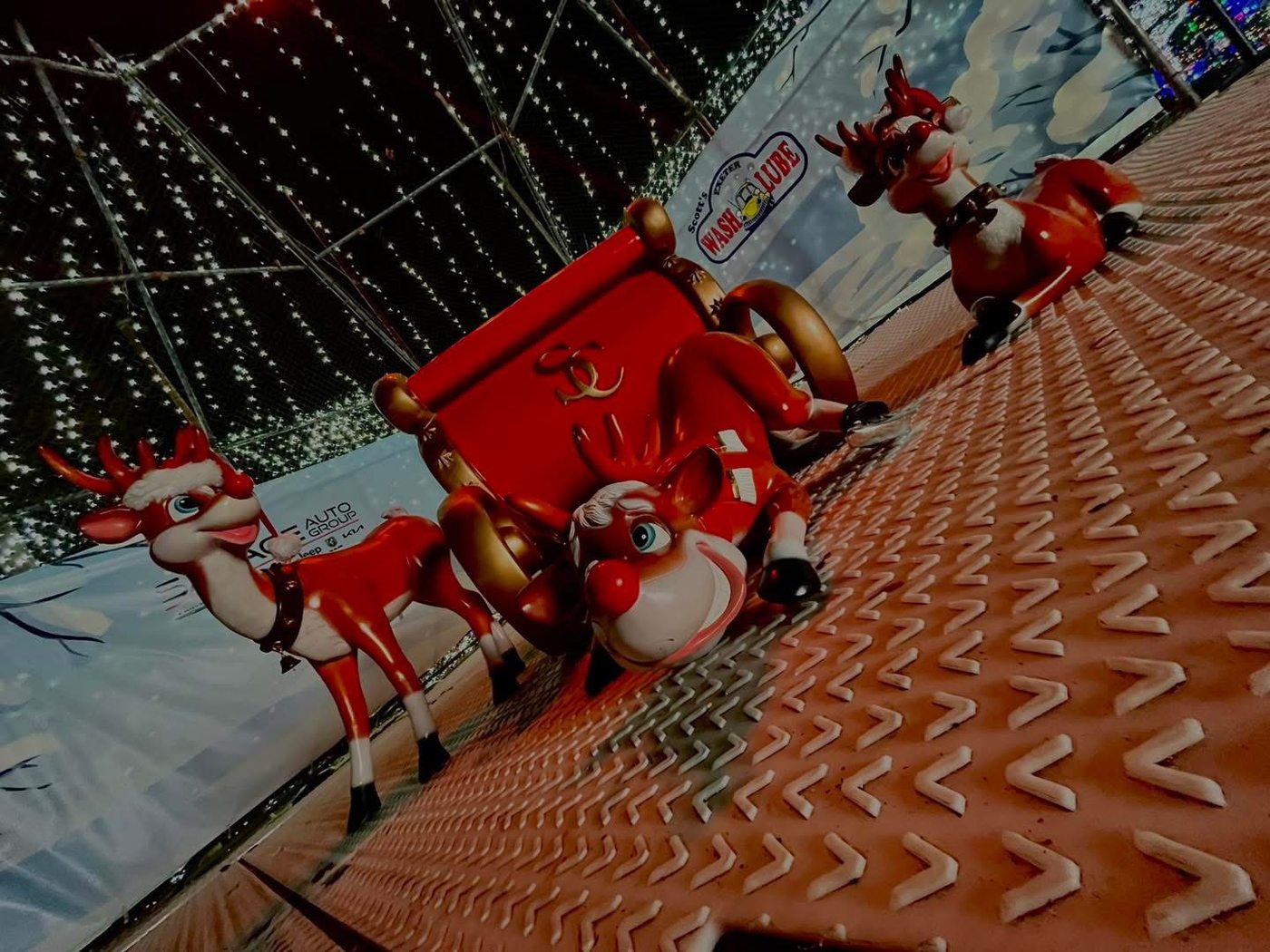 A sleigh and reindeer display with sponsor signs from an earlier season