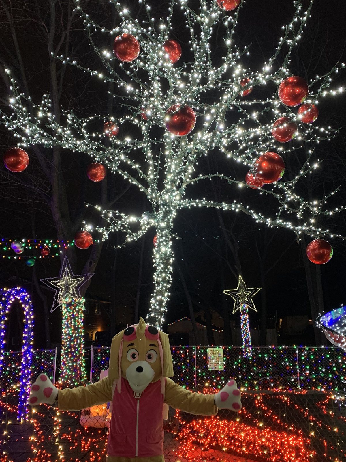 A costumed character beneath a white-lit tree with red ornaments at the display in a past season